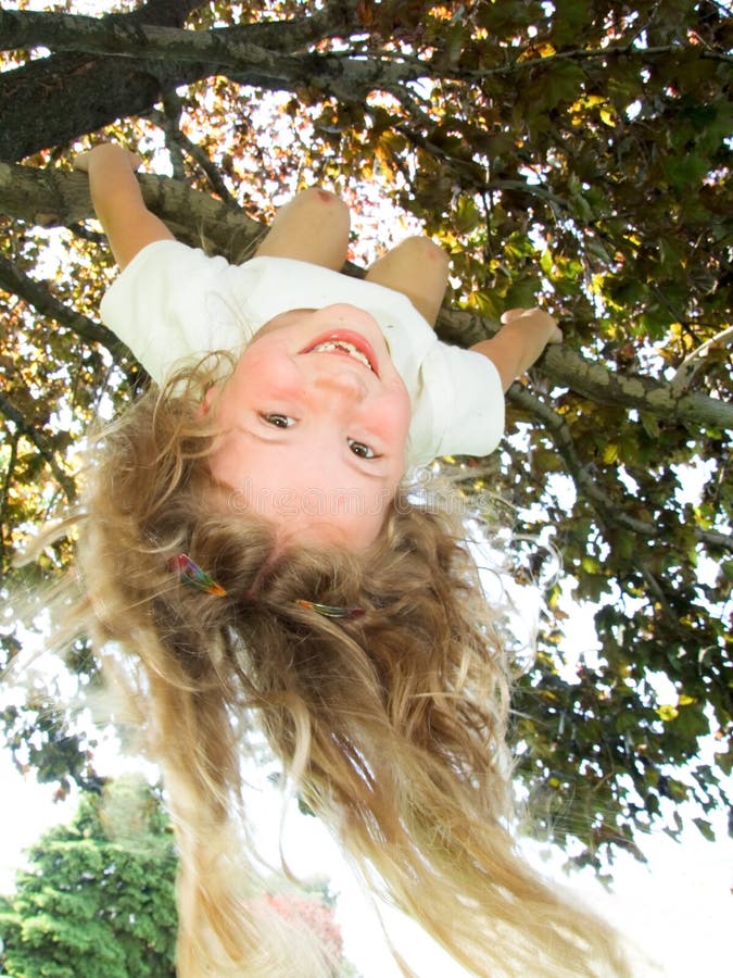 Ragazza graziosa con un grande sorriso appeso a testa in giù da un albero.