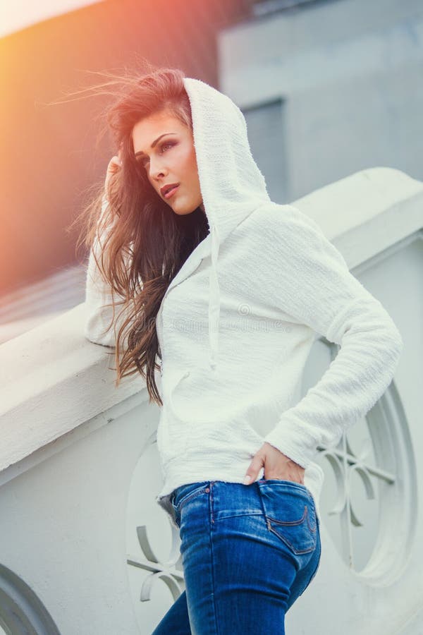 Urban girl  in blue jeans and white sweater  with hood  summer day in city