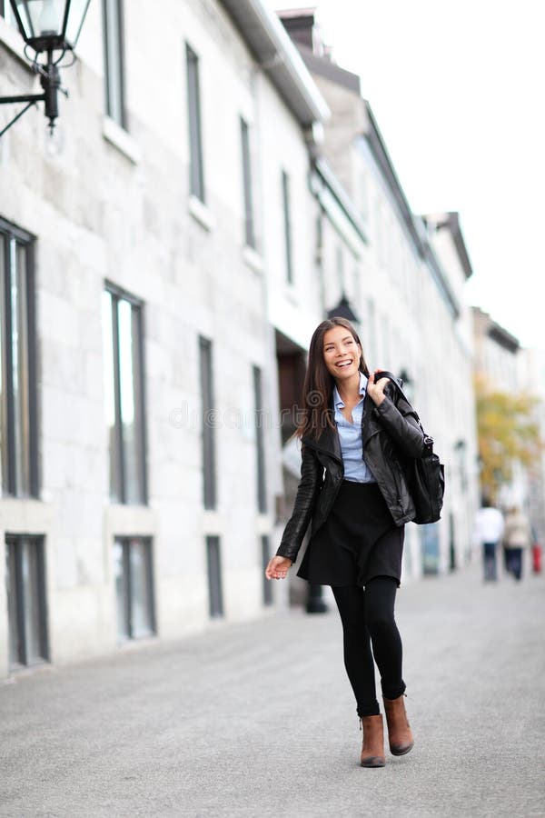 Urban modern woman outdoor walking in city street. Female fashion model wearing cool leather jacket and shoes outside. Happy ethnic Asian Caucasian girl in her twenties. Urban modern woman outdoor walking in city street. Female fashion model wearing cool leather jacket and shoes outside. Happy ethnic Asian Caucasian girl in her twenties.