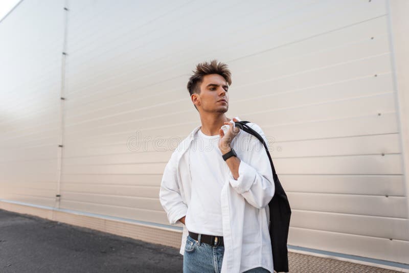 Urban Young Man Fashion Model with Trendy Hairstyle in a Vintage White Shirt  in Jeans with a Black Fabric Bag Relaxes on the Stock Image - Image of  hairstyle, shirt: 196744395