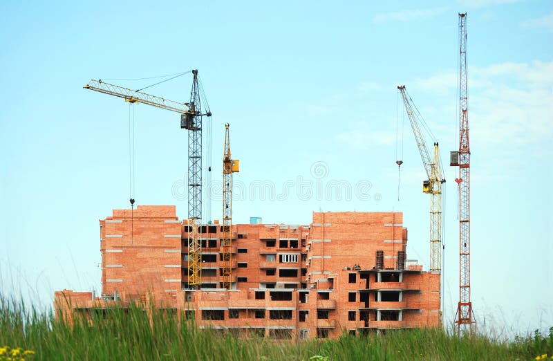 Residential building under construction and four cranes against the turquoise sky with some green grass at the foreground. Residential building under construction and four cranes against the turquoise sky with some green grass at the foreground