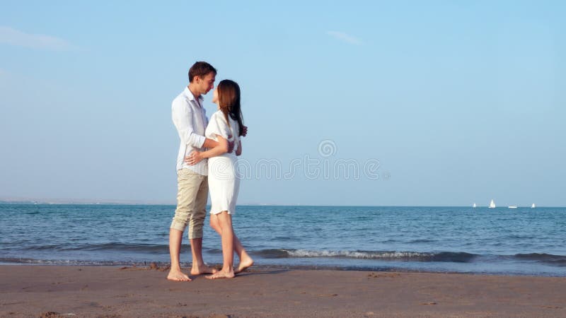 Urlopowa para przy plażą przy zmierzchu mienia romantycznymi rękami i całowaniem