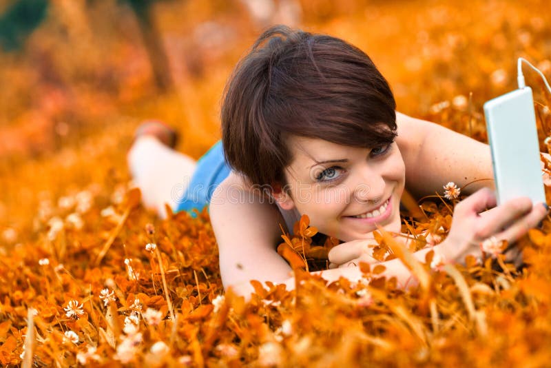 Cute charismatic young woman listening to music in a field of orange clover, in a tilted angle view as she smiles happily at the camera. Cute charismatic young woman listening to music in a field of orange clover, in a tilted angle view as she smiles happily at the camera