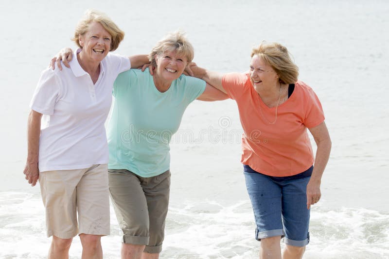 Lovely group of three senior mature retired women on their 60s having fun enjoying together happy walking on the beach smiling playful in female friendship and girlfriends on holidays concept. Lovely group of three senior mature retired women on their 60s having fun enjoying together happy walking on the beach smiling playful in female friendship and girlfriends on holidays concept