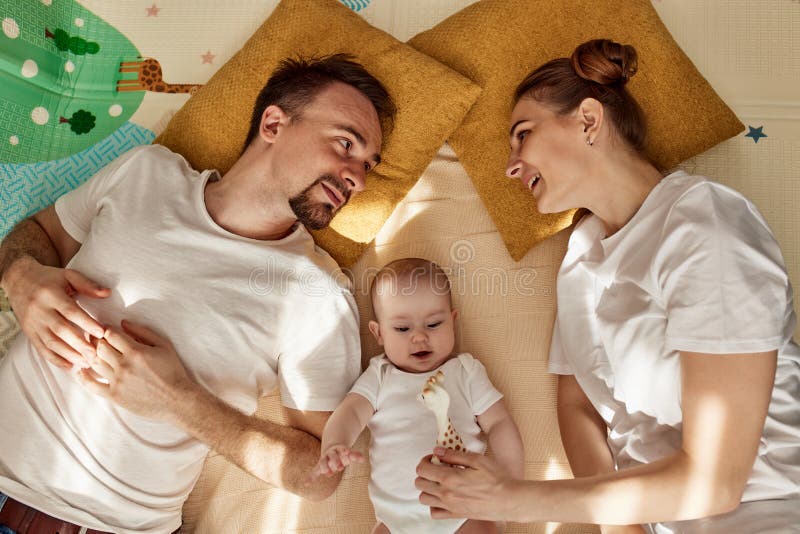 Urocze wesołe dziecko i jego rodzice leżą na podłodze w jasnym przytulnym pokoju z zabawkami. mama i tata przytulają się i całują zdjęcia royalty free