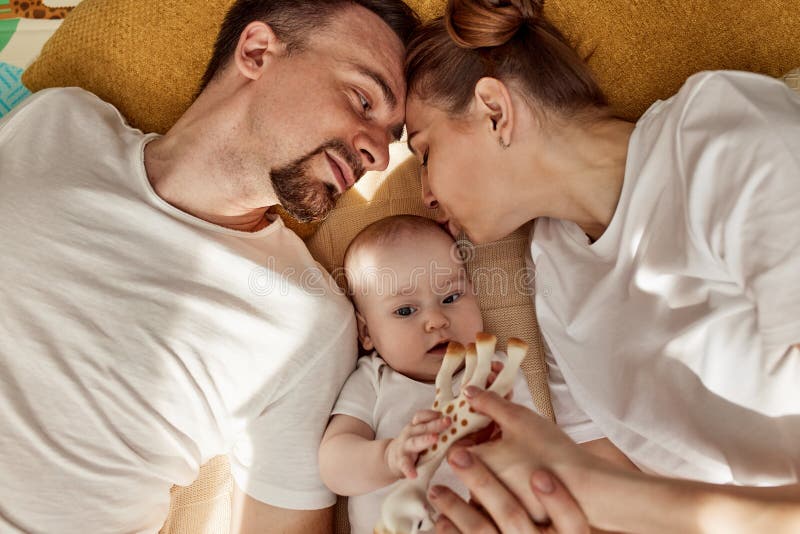 Urocze wesołe dziecko i jego rodzice leżą na podłodze w jasnym przytulnym pokoju z zabawkami. mama i tata przytulają się i całują fotografia royalty free