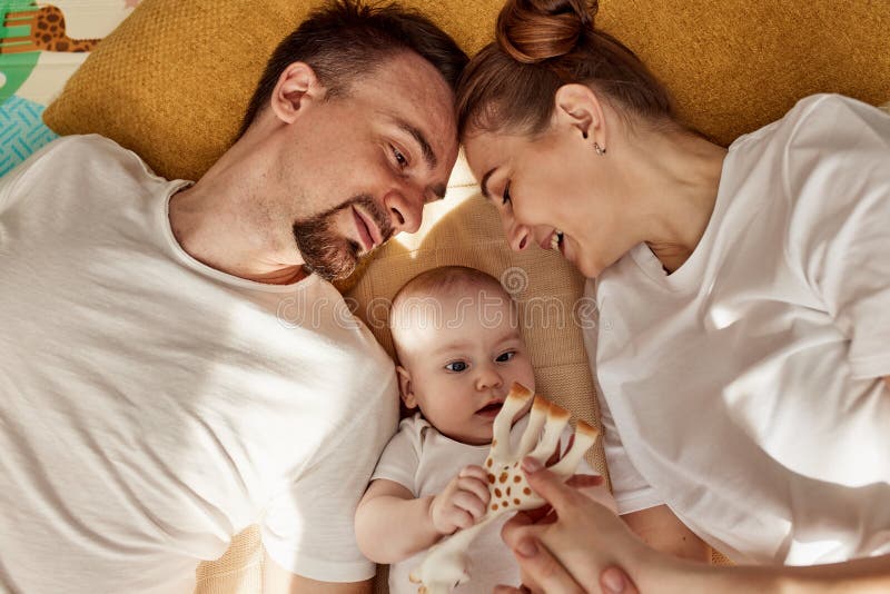 Urocze wesołe dziecko i jego rodzice leżą na podłodze w jasnym przytulnym pokoju z zabawkami. mama i tata przytulają się i całują zdjęcie royalty free
