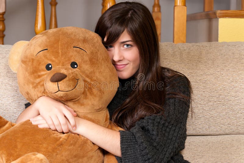 Urso de peluche do abraço da mulher nova que senta-se no sofá foto de stock royalty free Urso de peluche do abraço da mulher nova que senta-se no sofá foto de stock royalty free