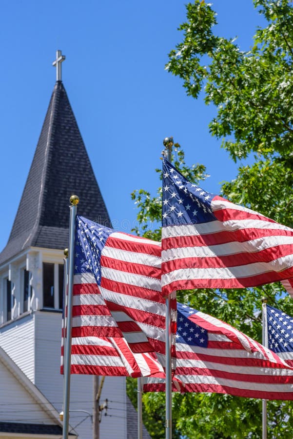 US flags waving outside white church steeple on Memorial Day