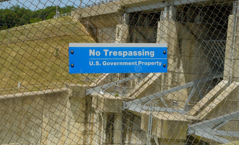 US government no trespassing sign posted om wired fence limiting access to a dam.