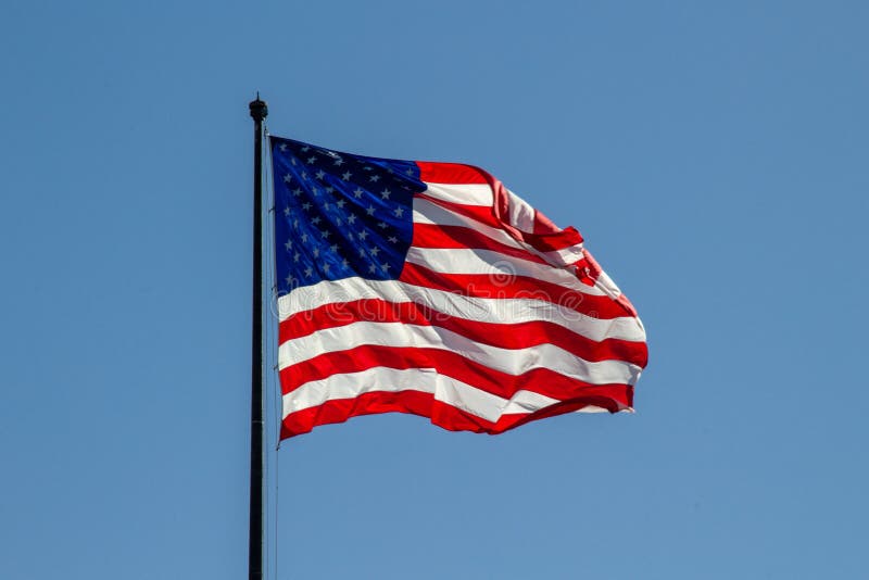 USA American flag waving in the wind on clear blue sky in background