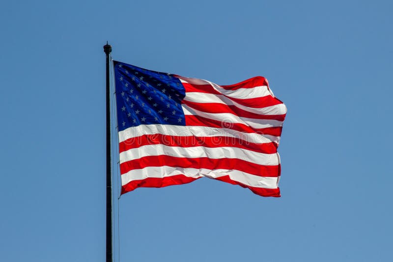 USA American flag waving in the wind on clear blue sky in background