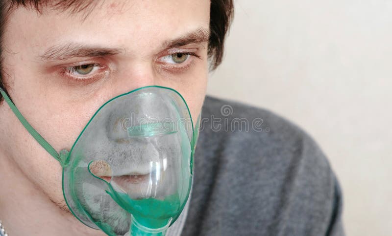Use nebulizer and inhaler for the treatment. Closeup young man`s face inhaling through inhaler mask. Front view. royalty free stock photography Use nebulizer and inhaler for the treatment. Closeup young man`s face inhaling through inhaler mask. Front view. royalty free stock photography