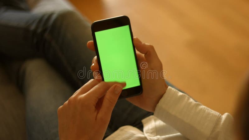 The user holds a smartphone with a green screen and scrolls down stock footage