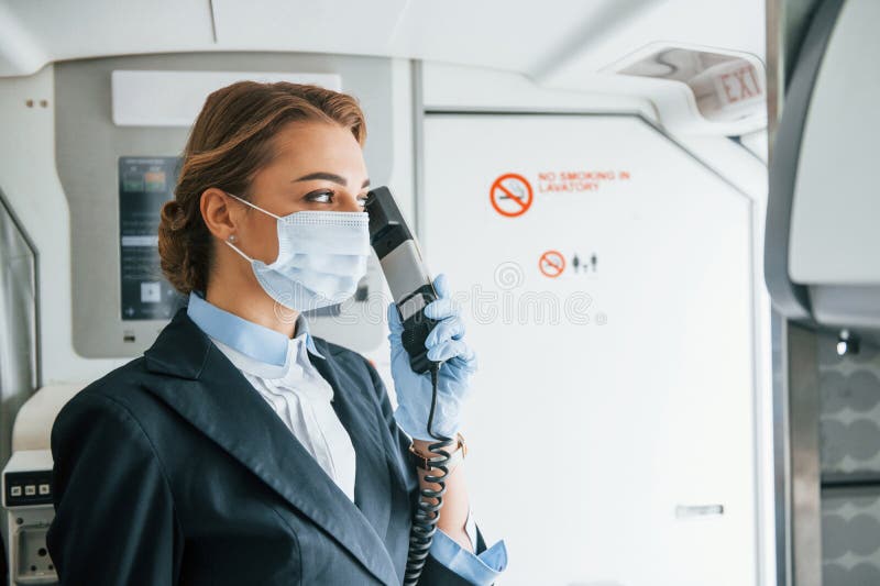 Uses Phone. Young Stewardess on the Work in the Passanger Airplane