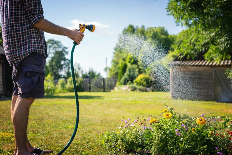 Usines d'arrosage de jeune homme de hippie dans une maison de campagne, un été et un soin de jardin images stock Usines d'arrosage de jeune homme de hippie dans une maison de campagne, un été et un soin de jardin images stock
