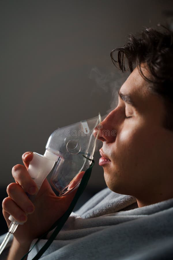 Using compressor nebulizer for disease treatment at home. Man inhaling through oxygen mask for cough treatment. stock images