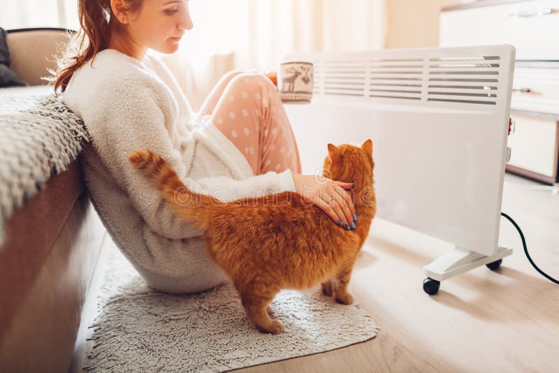 Using heater at home in winter. Woman warming and drinking tea with cat. Heating season