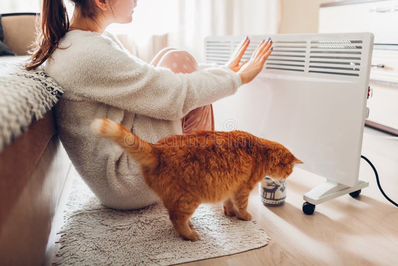 Using heater at home in winter. Woman warming her hands with cat. Heating season royalty free stock images