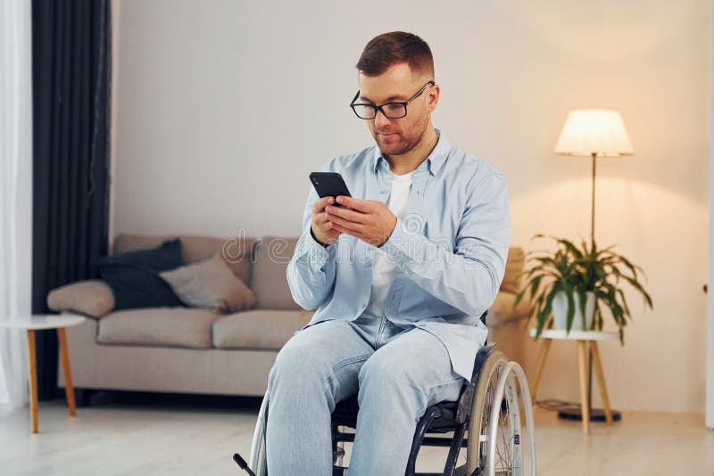 Using Phone. Disabled Man in Wheelchair is at Home Stock Photo Image