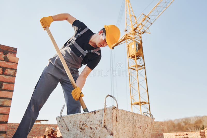 Using Showel. Construction Worker in Uniform and Safety Equipment Have Job on Building Stock