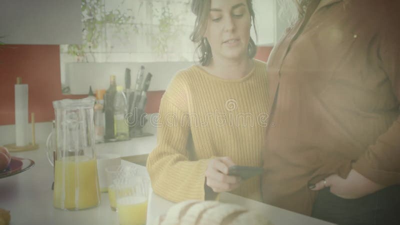 Using smartphone, person in kitchen with juice and bread, other watching animation stock video footage