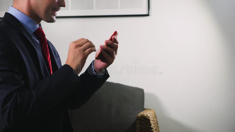 Uso alegre bonito um smartphone celular ao sentar-se na sala de visitas na noite Homem novo de sorriso feliz foto de stock royalty free Uso alegre bonito um smartphone celular ao sentar-se na sala de visitas na noite Homem novo de sorriso feliz foto de stock royalty free