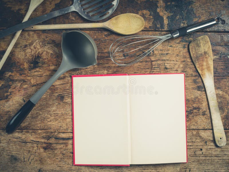 A selection of kitchen utensils on a wooden table with an open book. A selection of kitchen utensils on a wooden table with an open book