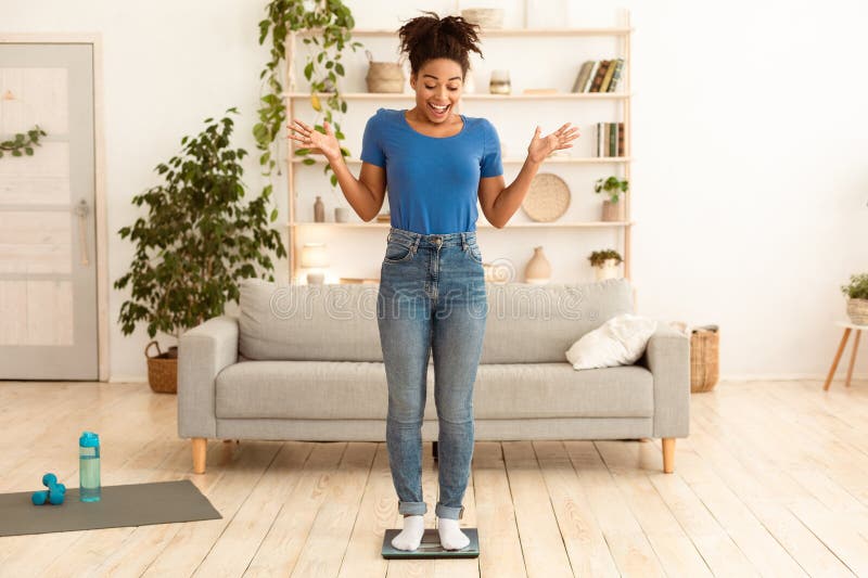 Utmärkt Slim Black Girl som står på WeightScales i full längd hemma royaltyfri foto