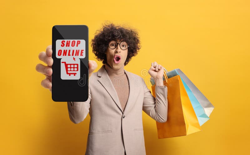 Utmärkt ung man med glasögon som håller shoppingväskor och en smartphone med app för onlineshopping royaltyfria bilder