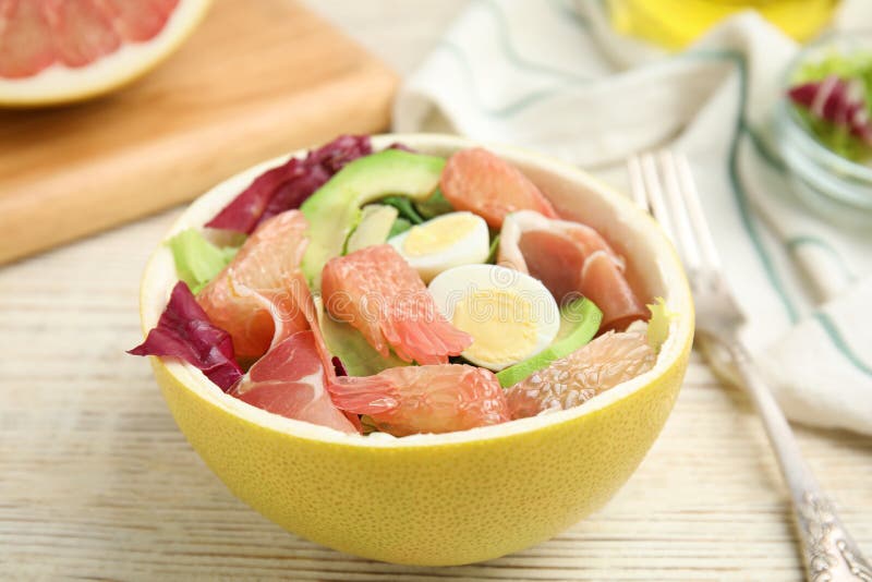 Utsökt pomelosallad med prosciutto i halva frukt på en vit bordsduk av trä arkivfoton