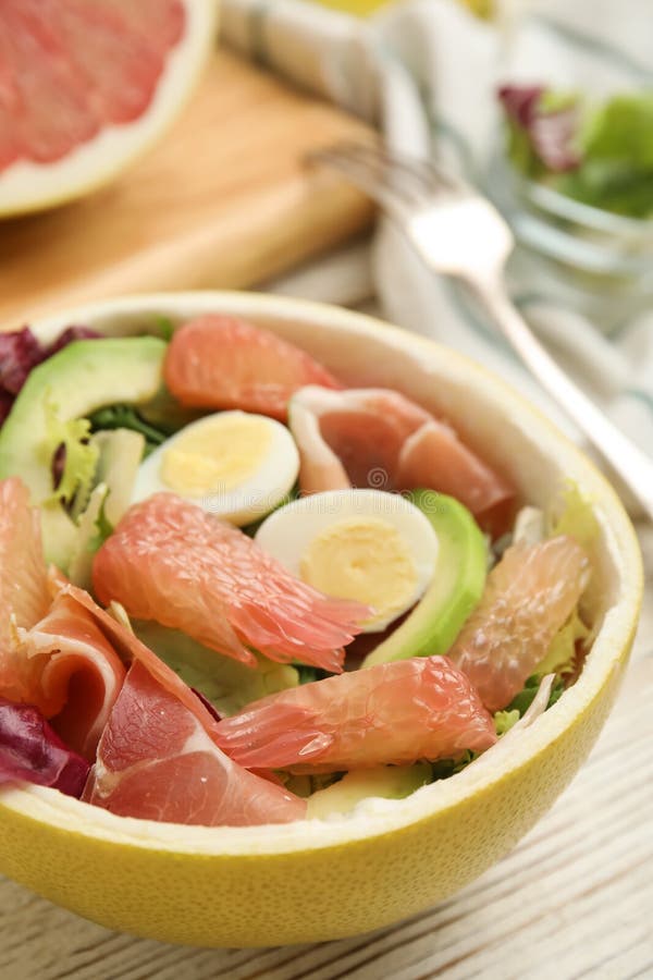 Utsökt pomelosallad med prosciutto i halva frukt på en vit bordsduk av trä arkivfoto