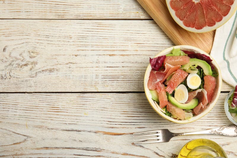 Utsökt pomelosallad med prosciutto i hälften av frukten på det platta vita träbordet. utrymme för text royaltyfria foton