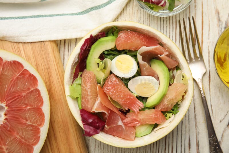Utsökt pomelosallad med prosciutto i hälften av frukten på det platta vita träbordet arkivbilder