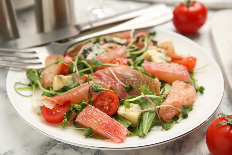 Utsökt pomelosallad med prosciutto serverad på vit marmor bordsduk arkivbild