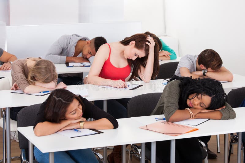 Uttråkad student med klasskompisar som sover på skrivbordet