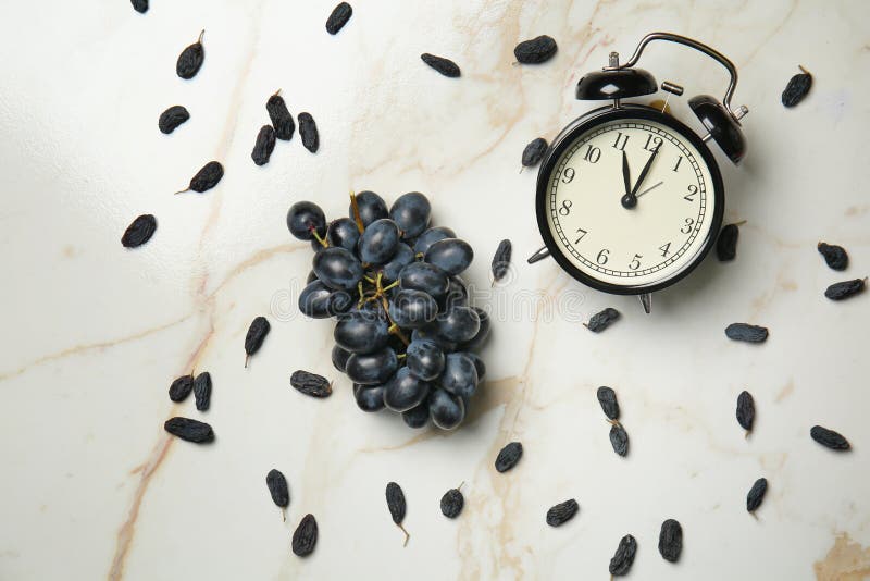 Uvas dulces maduras con las pasas y el despertador en la tabla ligera foto de archivo libre de regalías Uvas dulces maduras con las pasas y el despertador en la tabla ligera foto de archivo libre de regalías