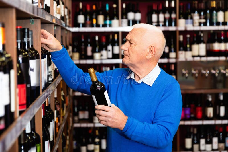 Uważny emeryt wybiera czerwone wino w sklepie z alkoholem fotografia stock