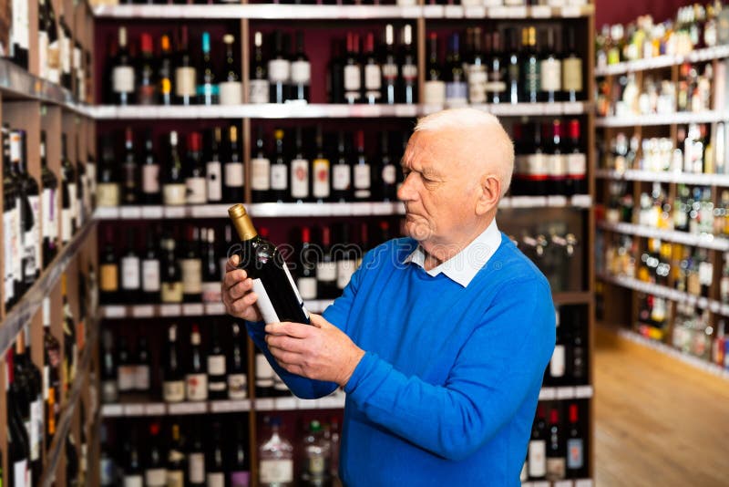 Uważny emeryt wybiera czerwone wino w sklepie z alkoholem zdjęcie royalty free