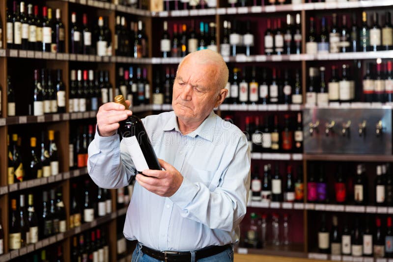 Uważny emeryt wybiera czerwone wino w sklepie z alkoholem zdjęcia stock