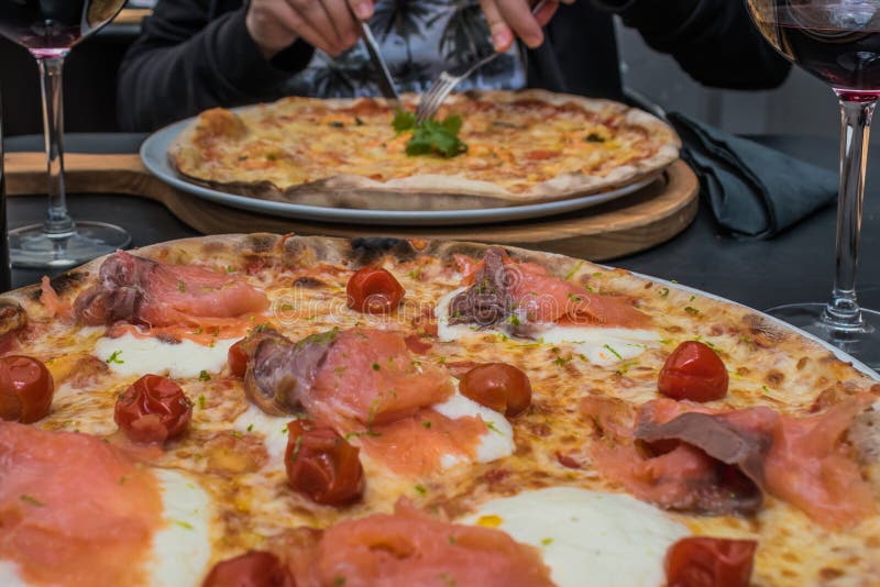 Uwędzona łososiowa pizza, czereśniowy pomidor i burrata ser z inną pizzą w plamie jako tło, typowy włoski jedzenie zdjęcie stock Uwędzona łososiowa pizza, czereśniowy pomidor i burrata ser z inną pizzą w plamie jako tło, typowy włoski jedzenie zdjęcie stock