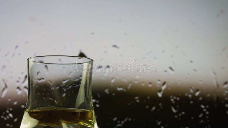 Uísque num copo contra o fundo de uma janela de chuva um copo de uísque armado filmando chuva fora da janela.