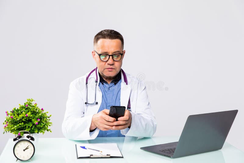 Uśmiechający się lekarz mężczyzny korzystający z telefonów komórkowych i pracujący na laptopie w sali medycznej w szpitalu obraz stock