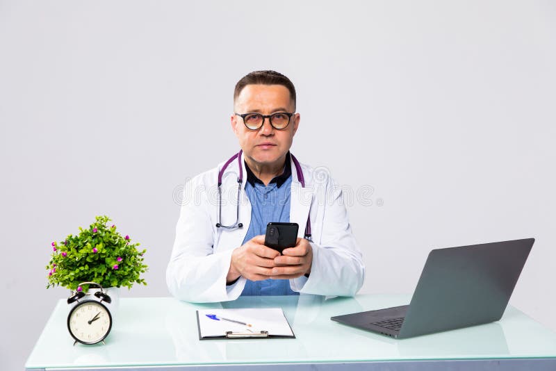 Uśmiechający się lekarz mężczyzny korzystający z telefonów komórkowych i pracujący na laptopie w sali medycznej w szpitalu zdjęcia stock