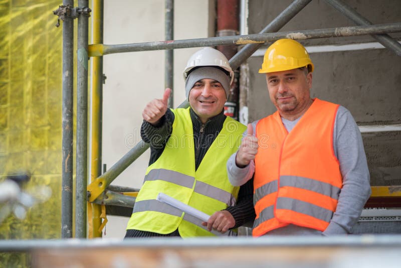 Uśmiechnięci i pomyślni pracownicy budowlani pozuje pokazywać aprobatę gestykulują fotografia stock Uśmiechnięci i pomyślni pracownicy budowlani pozuje pokazywać aprobatę gestykulują fotografia stock