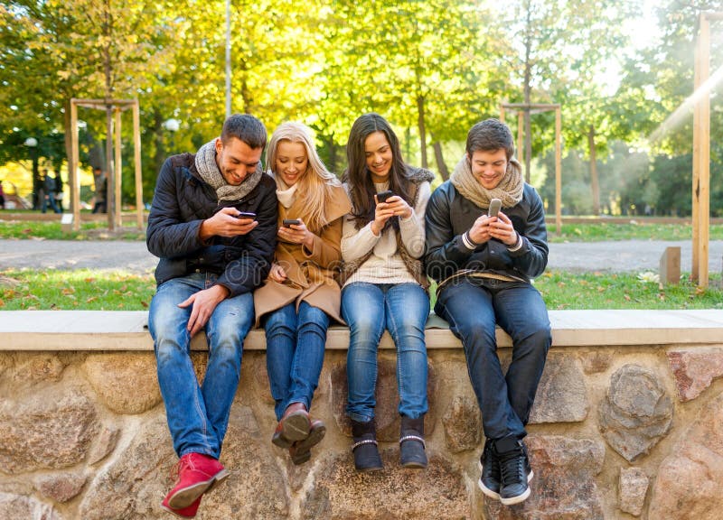 Uśmiechnięci przyjaciele z smartphones w miasto parku obrazy stock
