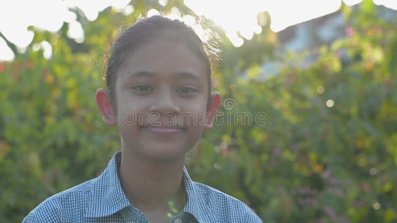 Uśmiechnięta azjatycka urocza dziewczynka patrząca na kamerę, stojąca na dziedzińcu pod porannym słońcem.