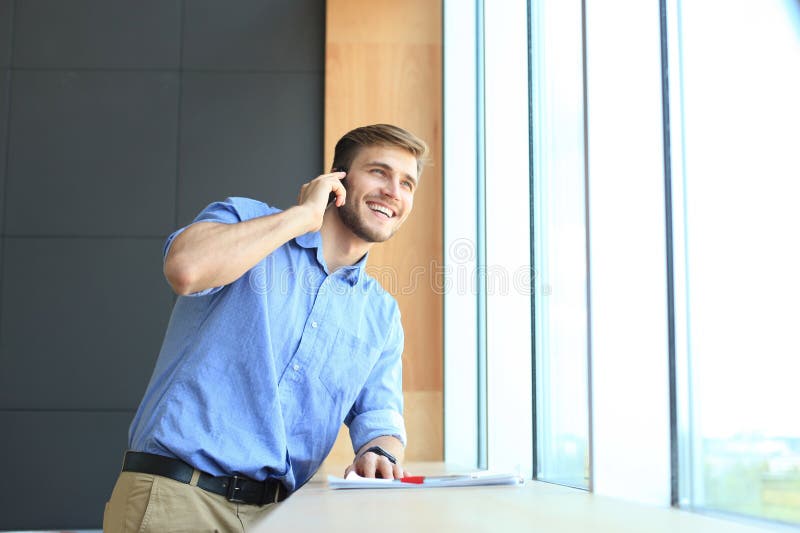 Uśmiechnięta biznesmen pozycja i używać telefon komórkowy w biurze zdjęcia stock Uśmiechnięta biznesmen pozycja i używać telefon komórkowy w biurze zdjęcia stock