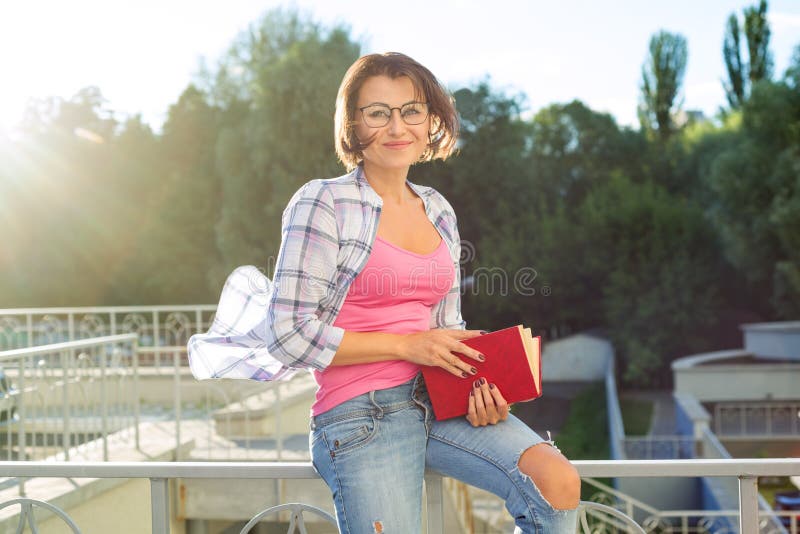 Uśmiechnięta brunetka relaksuje outdoors i czytelnicza książka zdjęcia royalty free Uśmiechnięta brunetka relaksuje outdoors i czytelnicza książka zdjęcia royalty free