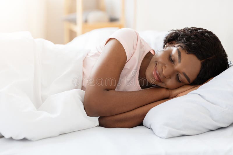 Healthy sleeping, sleep hygiene concept. Smiling pretty young black woman sleeping in her bed at home, copy space. African american lady having nap, resting in white cozy bedroom. Healthy sleeping, sleep hygiene concept. Smiling pretty young black woman sleeping in her bed at home, copy space. African american lady having nap, resting in white cozy bedroom